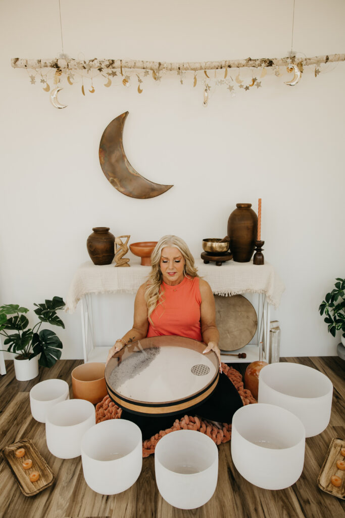 Wide shot of women's wellness coach seated on the floor in front of crystal singing bowls and crescent moon wall art during Minneapolis brand photography session