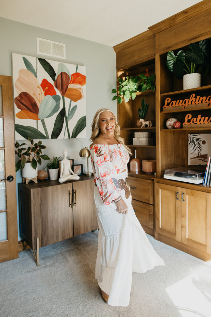 Women's mentor posing in front of large floral wall art and wooden shelving during brand photography session