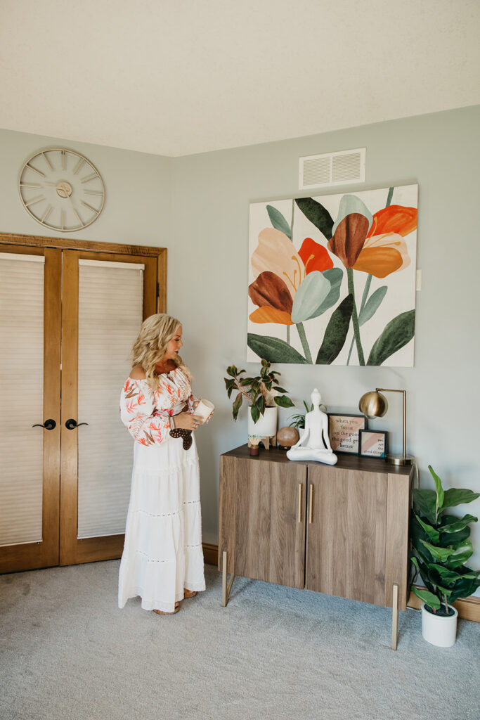 Women's wellness coach laughing beside wooden cabinet and Laughing Lotus branded bookcase during brand shoot