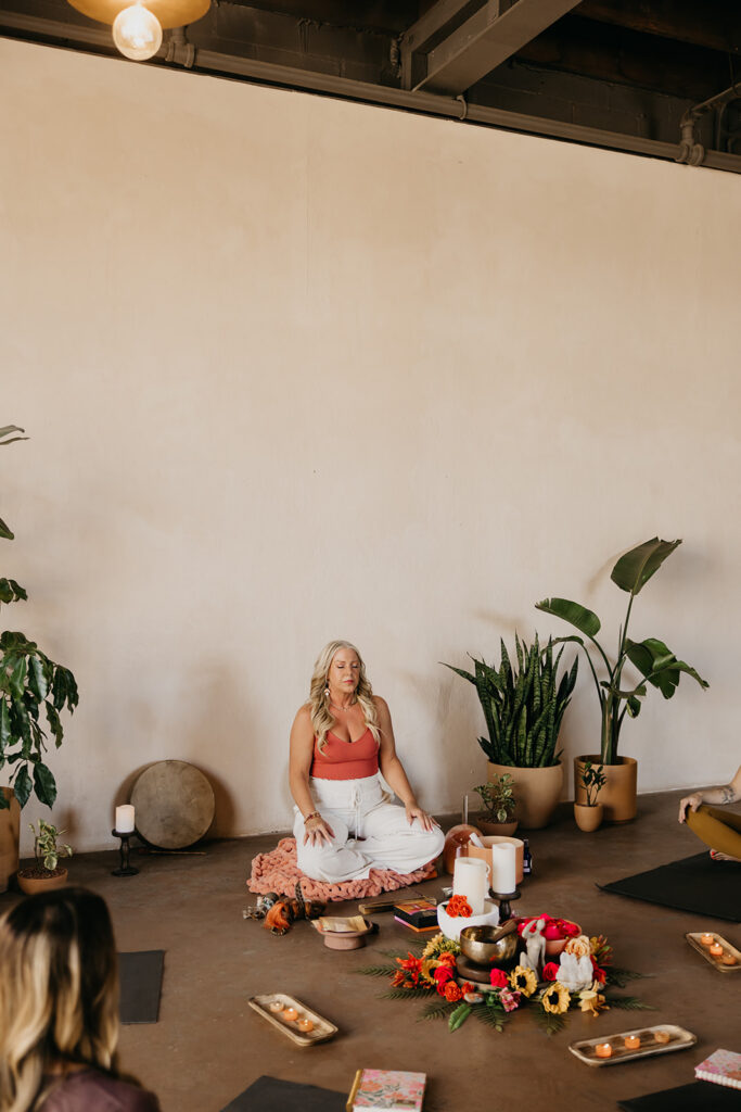Women's wellness coach in white seated in meditation in an open light-filled retreat space during brand photography session
