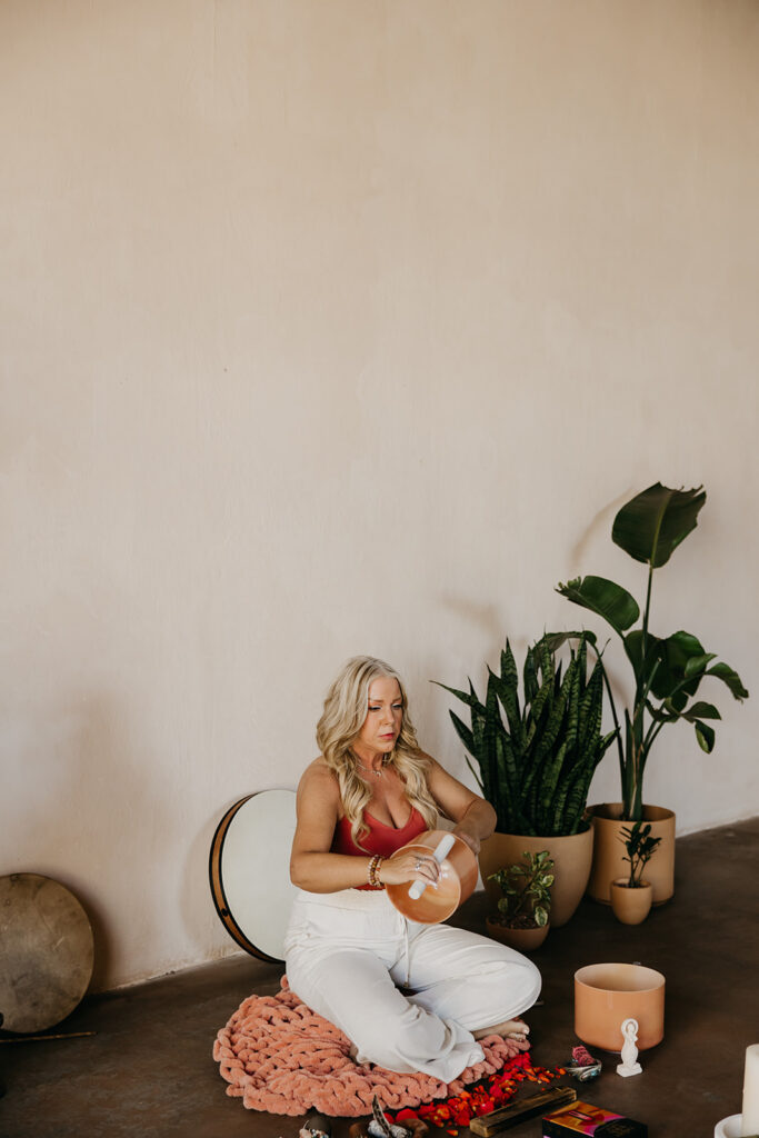 Women's mentor seated cross-legged beside a large monstera plant during brand photography shoot