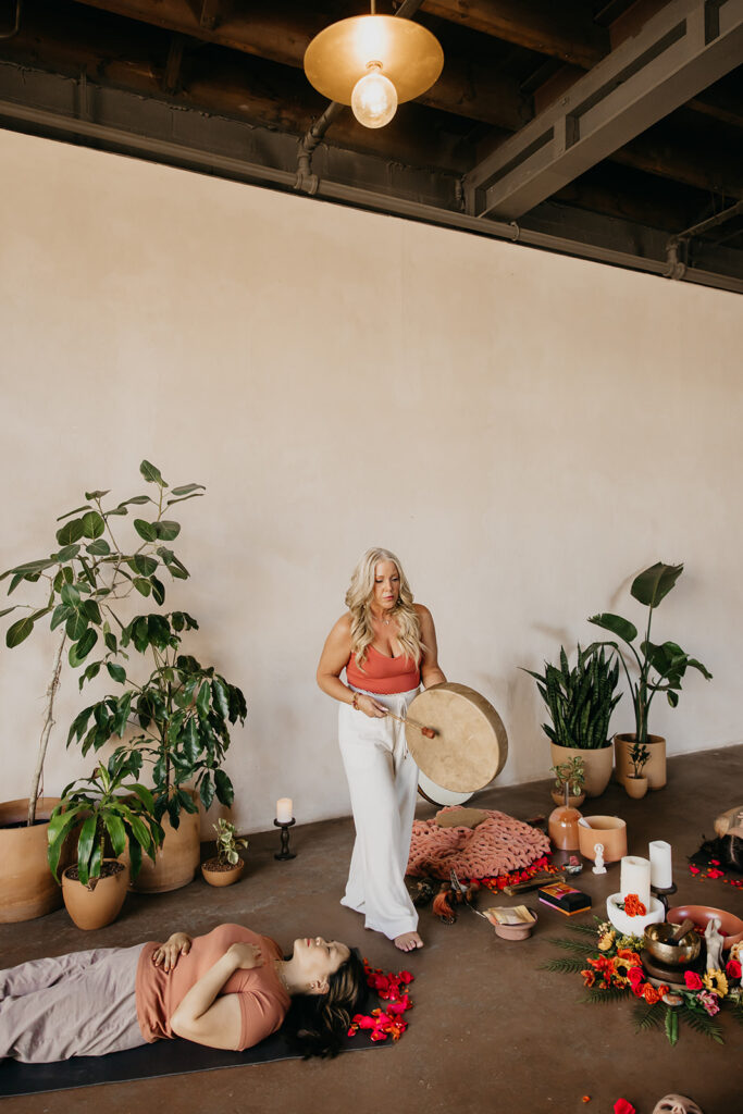 Women's wellness coach standing beside a large gong in a nature-filled retreat space during brand photo session