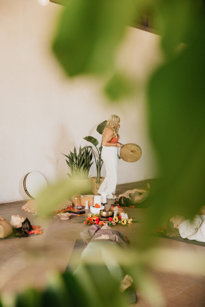 Wide shot through green foliage of women's wellness coach in a retreat setting during brand photography session