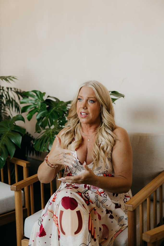 Women's wellness coach speaking expressively while seated in a wicker chair during brand photography session in Minneapolis