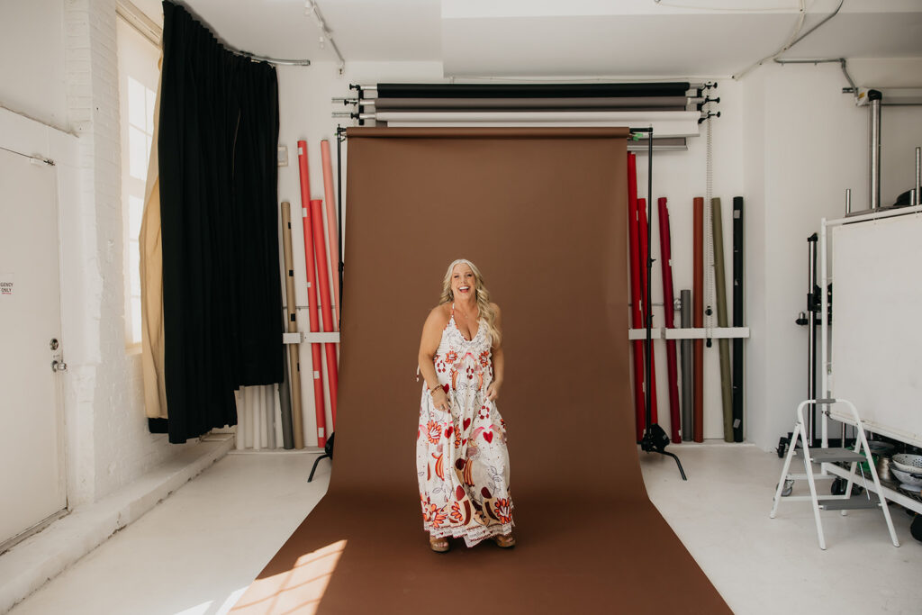Full-length shot of women's mentor in a floral maxi dress standing on a brown seamless backdrop in a Minneapolis photography studio