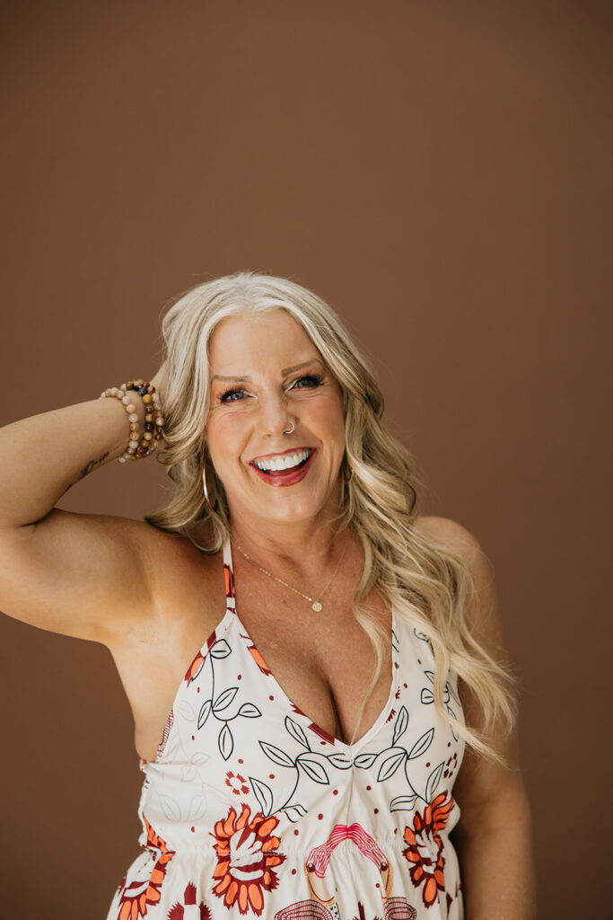 Women's wellness coach throwing her head back and laughing during brand photography session on brown studio backdrop