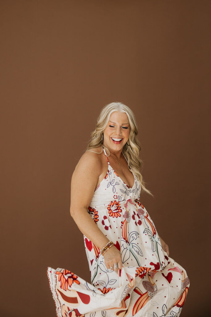 Women's wellness coach twirling in a floral dress on a brown backdrop during Minneapolis brand photography session