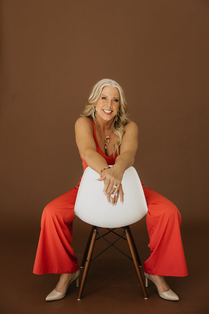 Women's mentor seated on a white chair smiling in an orange jumpsuit during brand photography session