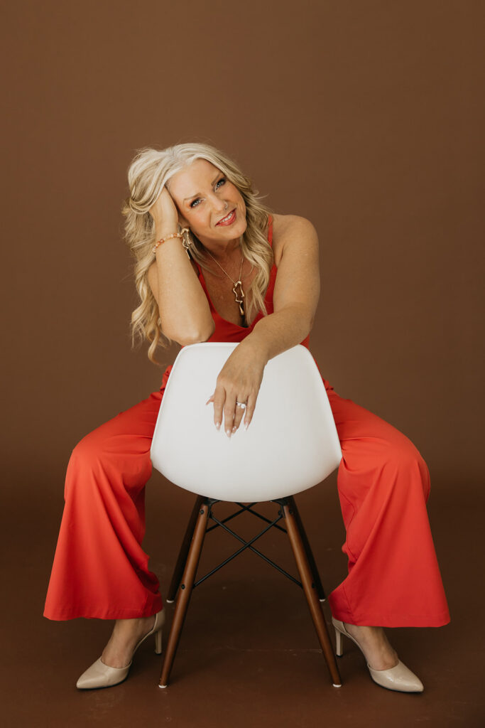Women's wellness coach leaning on the back of a white chair in an orange jumpsuit during brand photo shoot
