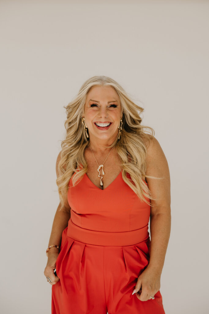 Women's wellness coach in an orange jumpsuit laughing against a white studio backdrop during Minneapolis brand photography session