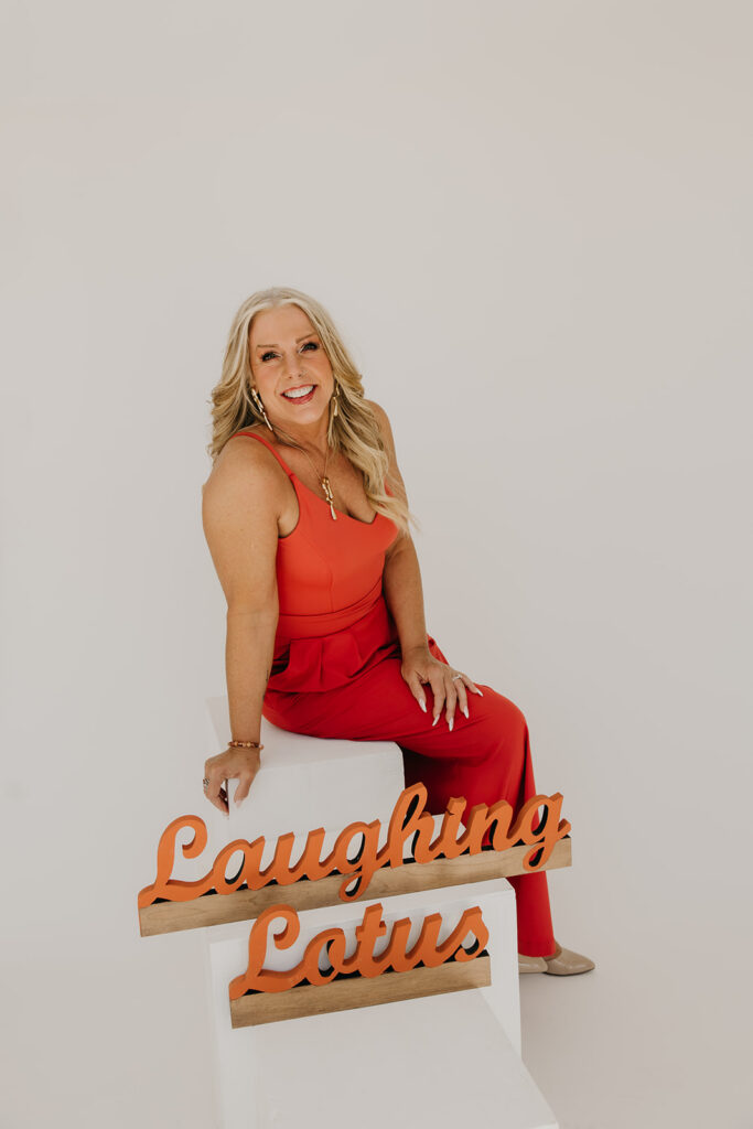 Women's mentor in orange jumpsuit seated on a white pedestal next to the Laughing Lotus sign during brand photo shoot
