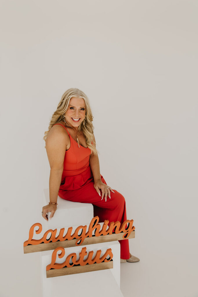 Women's wellness coach leaning against the Laughing Lotus branded sign during brand photography session on white studio backdrop