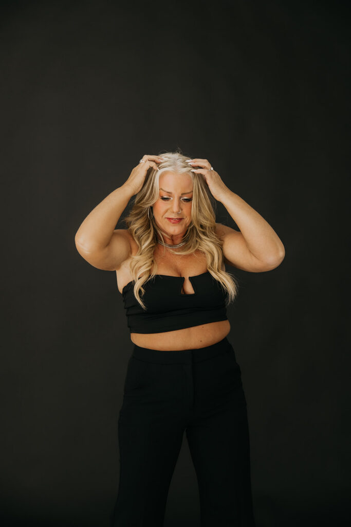 Women's wellness coach posing with hands in hair in a black crop top and wide-leg pants during brand photography session