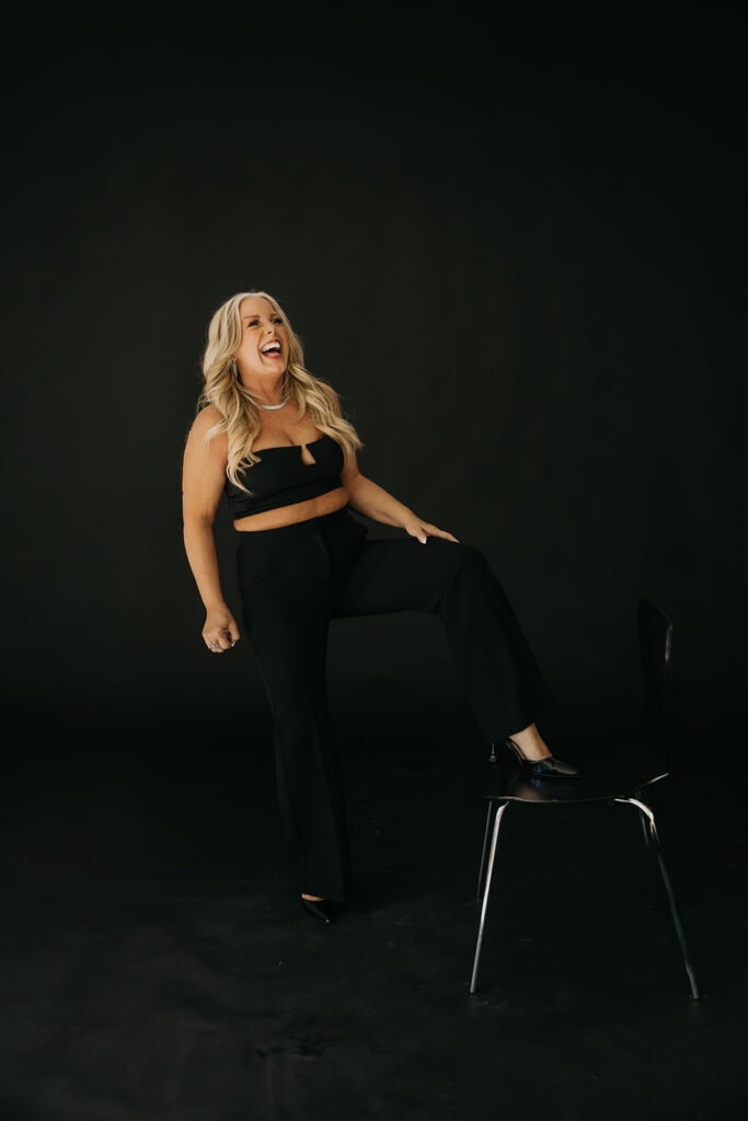 Women's mentor laughing while seated on a black chair during brand photography session