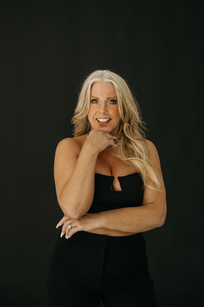 Women's wellness coach seated and leaning forward in a confident pose during brand photo shoot on dark backdrop