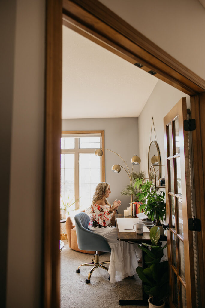 Wide shot of women's wellness coach working at her desk inside a bright home office during brand photography session