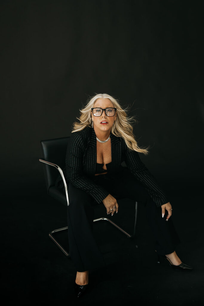 Women's mentor seated in a black chair wearing glasses and a blazer during brand photography session in Minneapolis