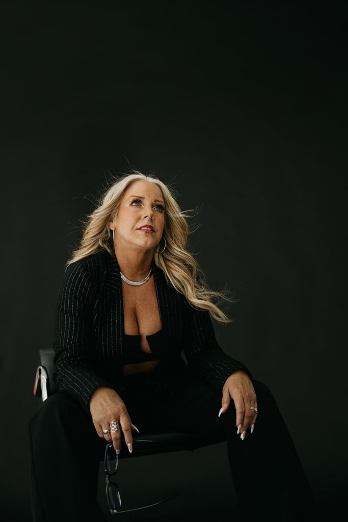 Women's mentor leaning back in a black chair during brand photography shoot on dark studio backdrop