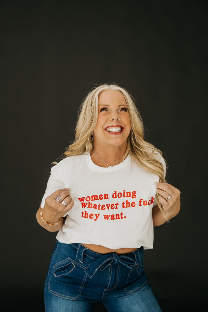 Women's wellness coach lifting her graphic tee and laughing during high-energy brand photography session in Minneapolis
