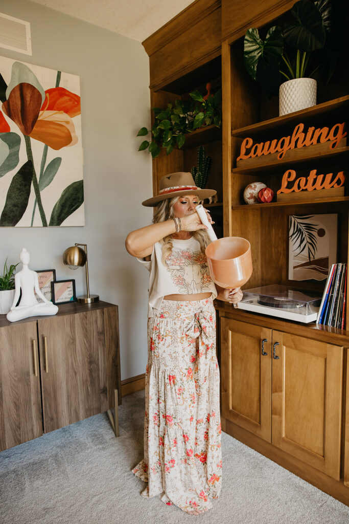 Women's energy healer holding a copper singing bowl in front of Laughing Lotus bookcase during brand photo shoot