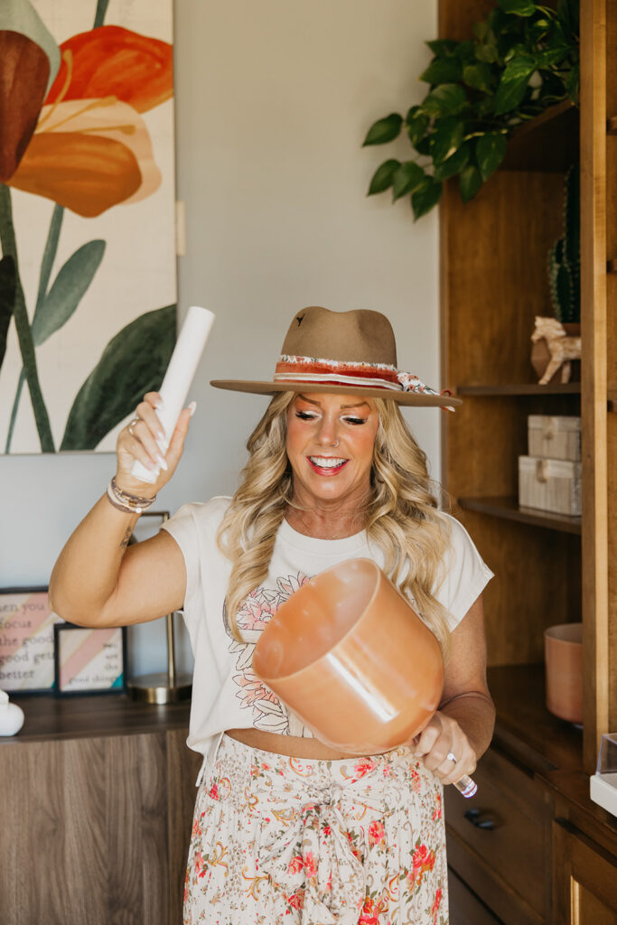 Women's wellness coach laughing while holding a singing bowl overhead in her healing studio during brand photography session