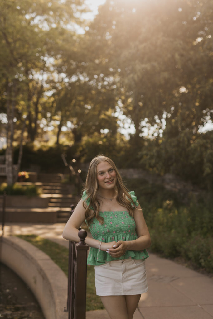 Hopkins senior photos of girl in green smocked top and white skirt walking on park path at golden hour
