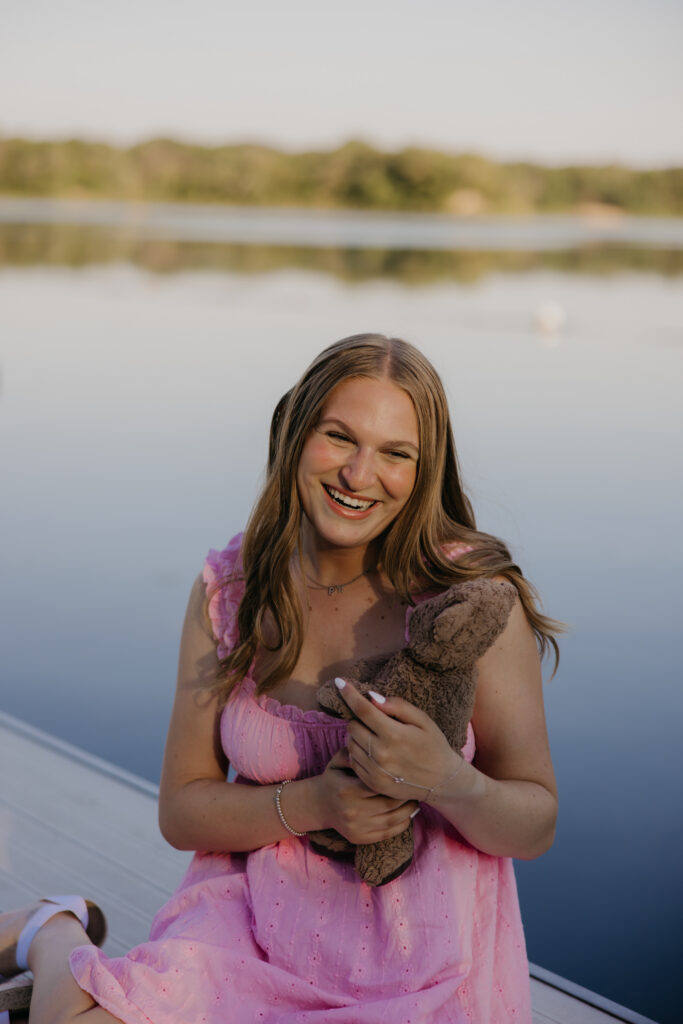 Hopkins senior photos of girl in pink mini dress on dock holding stuffed bunny with lake behind her