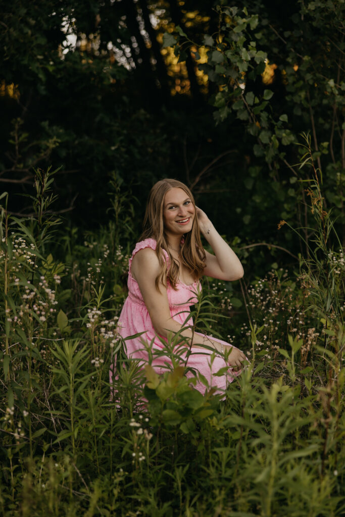 Hopkins High School senior girl in pink ruffle mini dress seated in wildflower field at golden hour