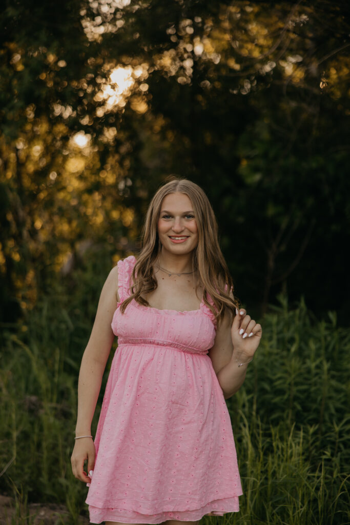 Hopkins senior photos of girl in pink mini dress standing among wildflowers at golden hour