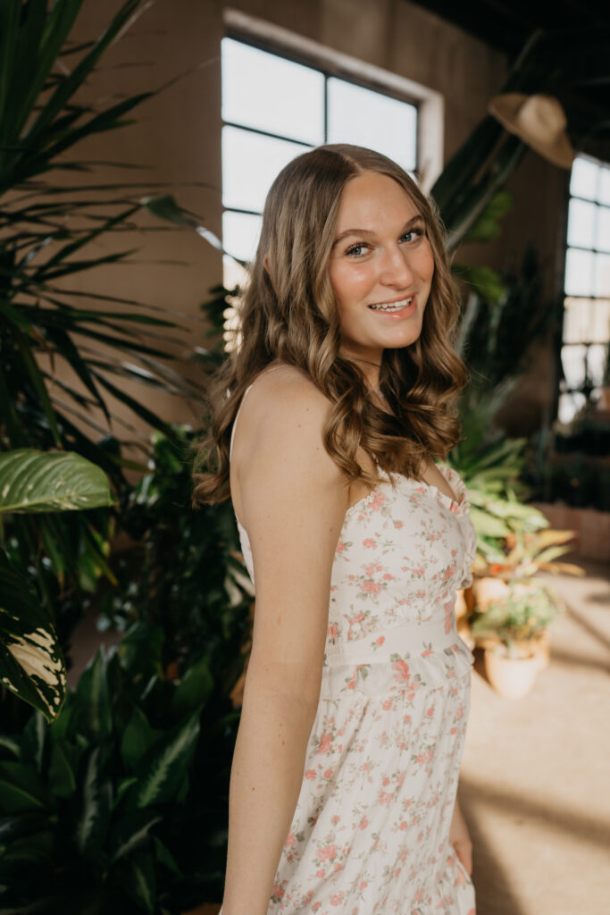 Hopkins senior photos side profile of girl smiling near sunlit window with plants in background