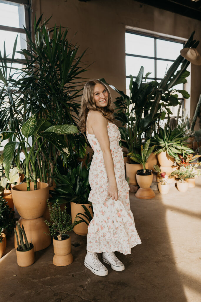 Hopkins senior photos of girl walking toward camera in floral dress near tall windows at Minneapolis plant shop