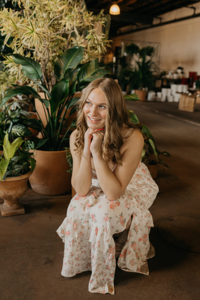 Hopkins senior photos of girl seated with chin on hands smiling at Minneapolis plant shop