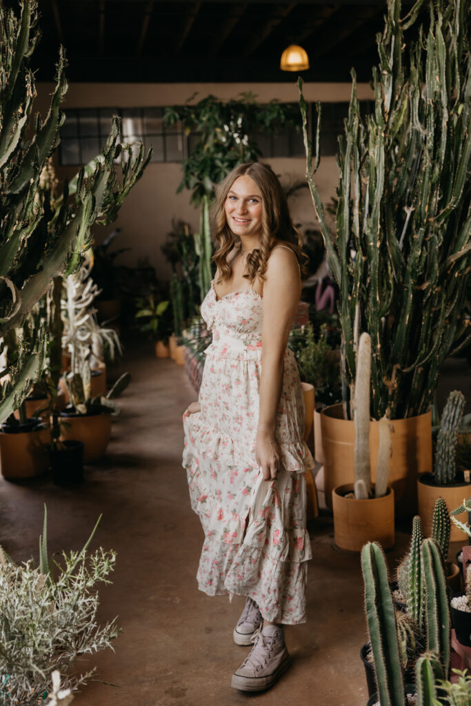 Hopkins High School senior girl in floral dress walking and smiling through cactus aisle at Minneapolis plant shop
