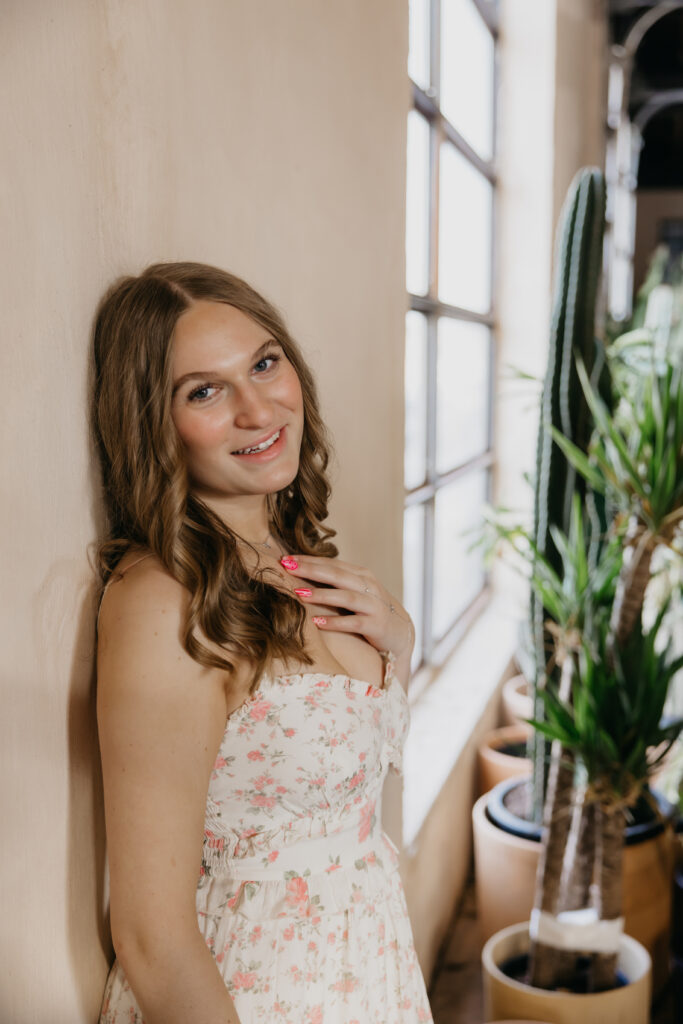 Hopkins senior photos close-up of girl in floral dress smiling by sunlit window with cactus behind her
