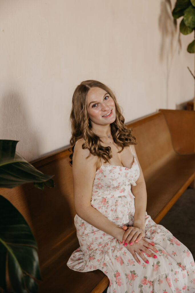 Hopkins senior photos of girl in floral dress seated on wooden pew at Minneapolis plant shop