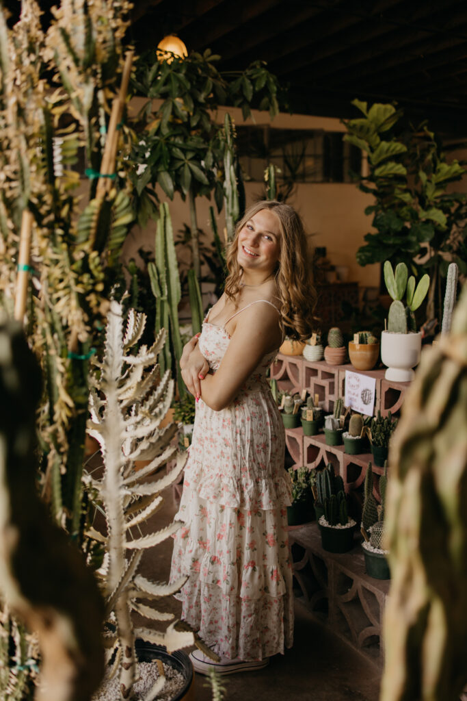 Hopkins senior photos of girl in floral maxi dress with arms crossed in cactus-filled Minneapolis plant shop