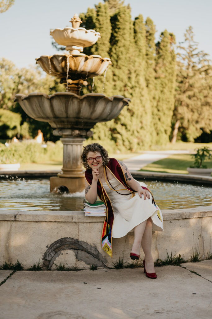 University of Minnesota grad sitting on stone fountain edge, playful pose, red heels visible