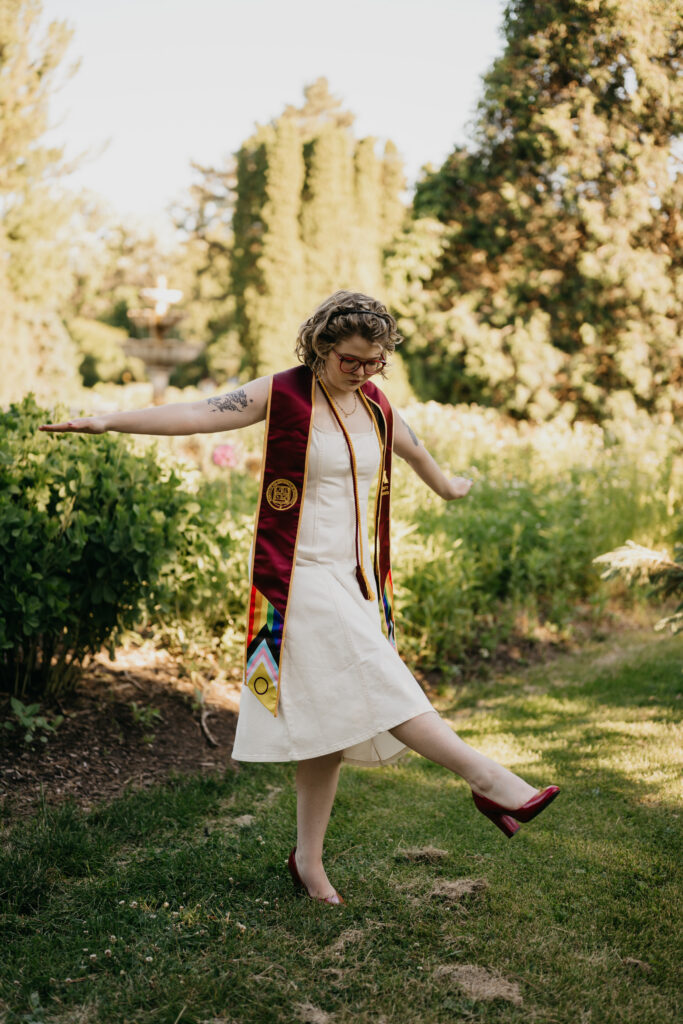 graduate mid-step in front of garden fountain, arms outstretched, dancing