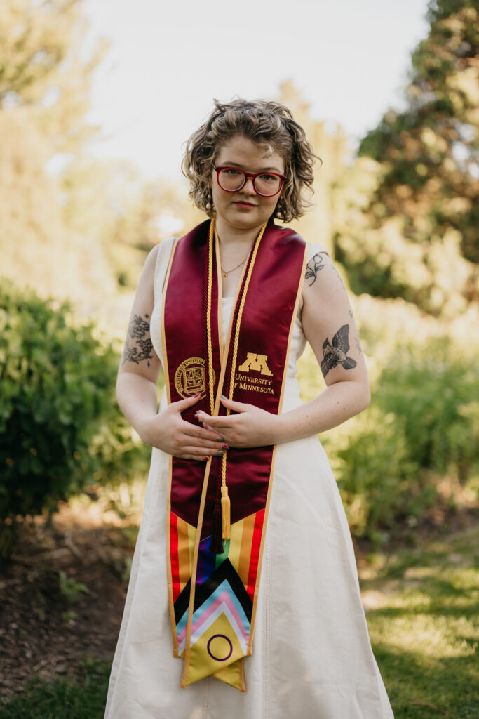 personalized graduation photoshoot Minnesota, graduate standing with hands clasped showing University of Minnesota stole