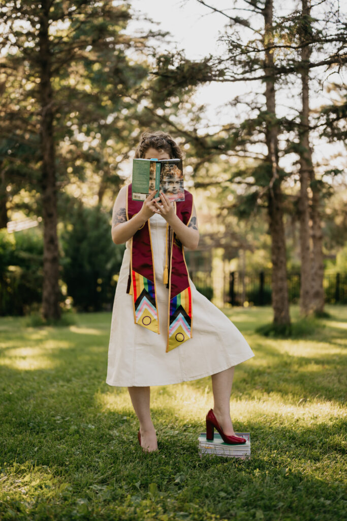 creative graduation photos Minneapolis, grad holding open book in front of her face on one leg
