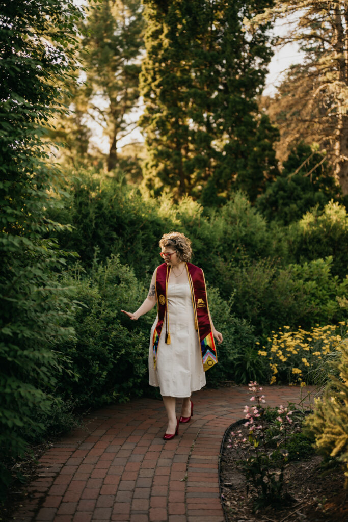 graduate walking a garden path, stole and dress in motion