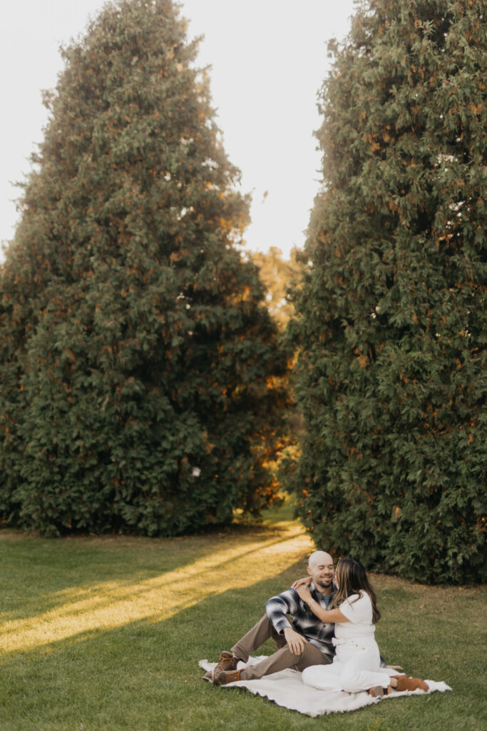 Couple sitting together on a blanket between tall evergreen trees