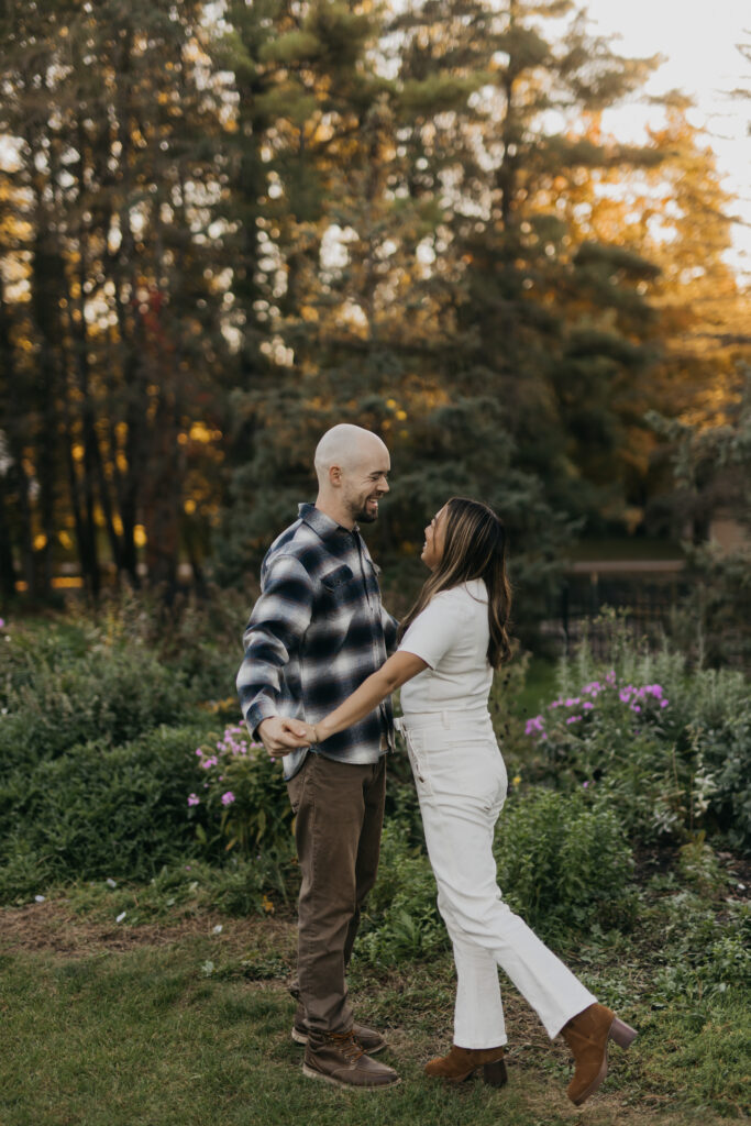 Couple holding hands and smiling at each other beside a flower garden