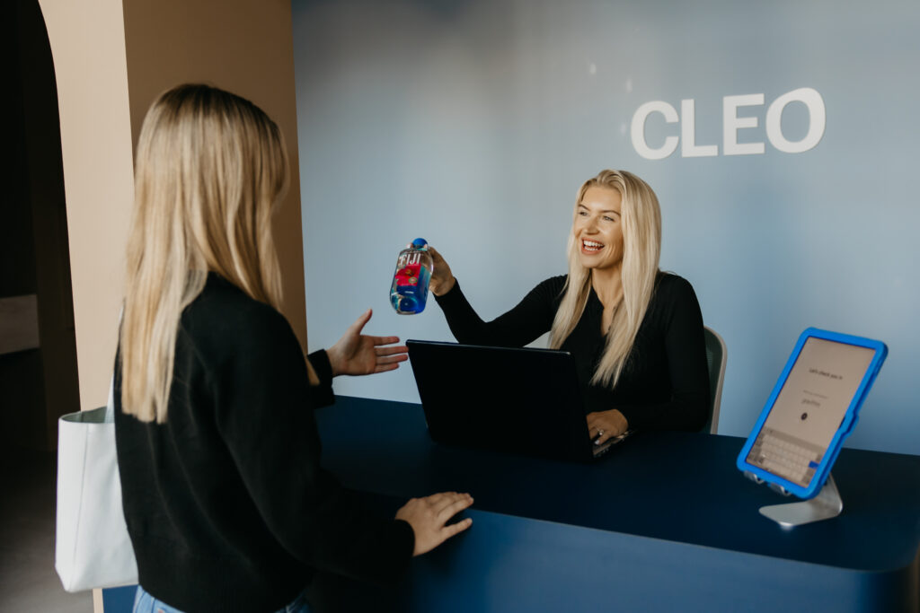 Team member laughing while holding a product next to a laptop, brand photography for CLEO Skin + Laser