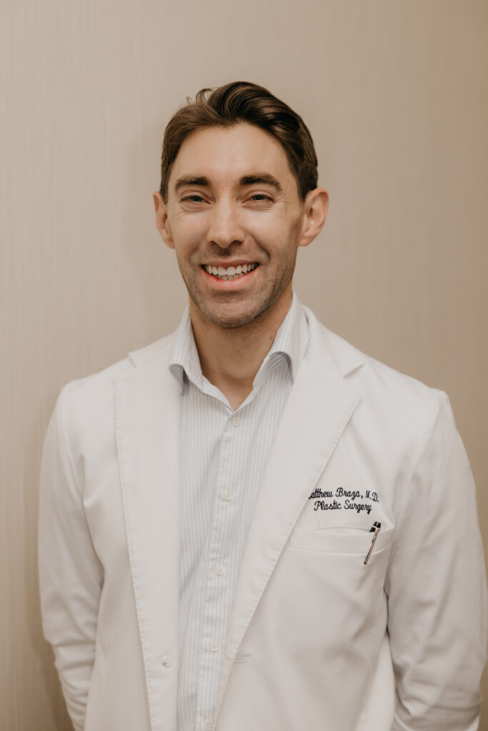 Dr. Matthew Braza in embroidered white coat smiling directly at camera in Edina practice