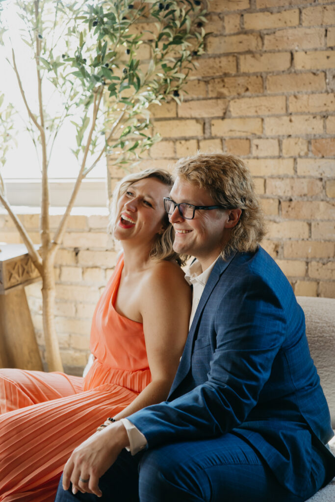 Candid laughing portrait of Dr. Mel Krug and a partner against a brick wall background