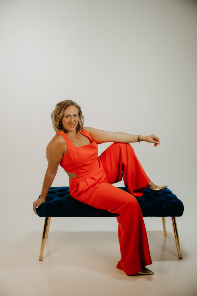 Woman seated on a blue velvet bench with arm extended, smiling at the camera