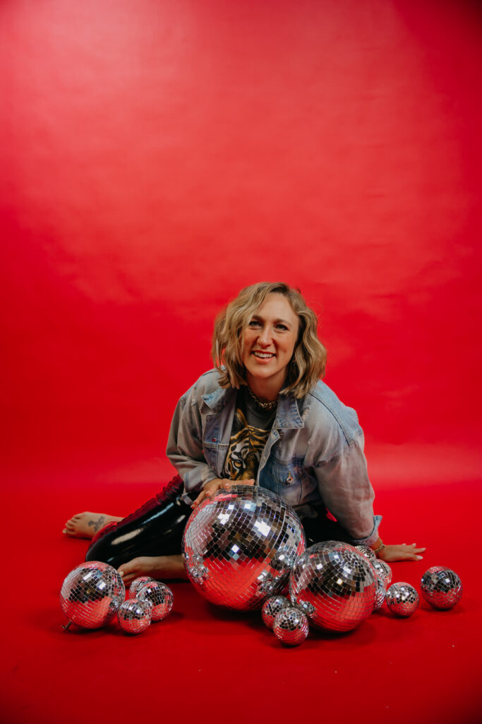 Woman seated on the ground laughing, disco balls scattered around her