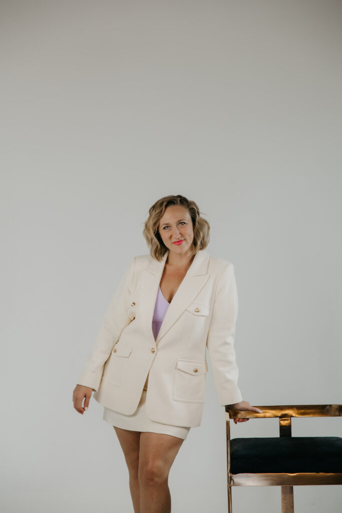 Standing portrait of Dr. Mel Krug in a cream blazer suit against a grey studio backdrop