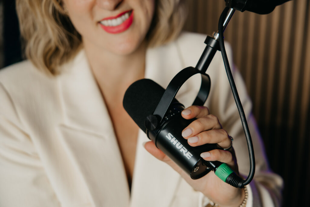 Close crop of Dr. Mel Krug in a cream blazer holding a Shure podcast microphone, brand photography for transformational coaches